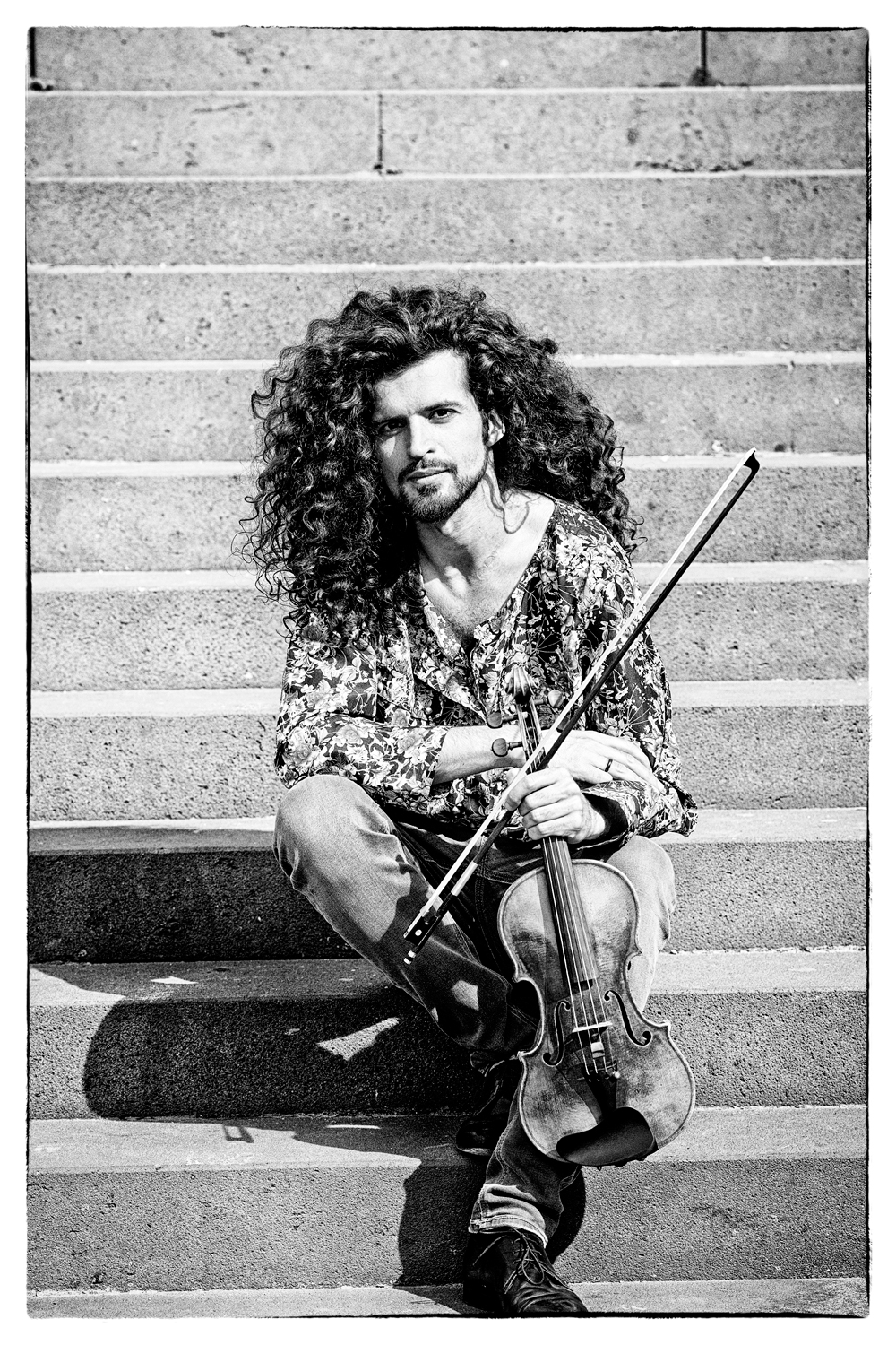 Puschan Mousavi Malvani auf einer Treppe mit Violine Geiger mit Violine sitzt auf einer Treppe und blickt in die Kamera.